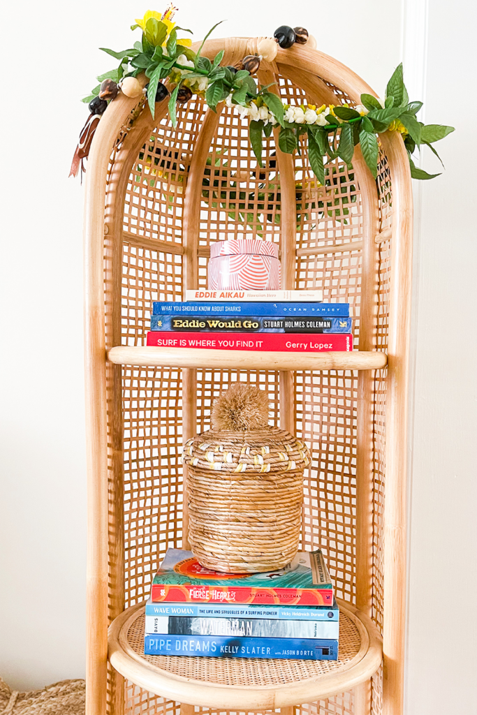 Surf books on rattan book shelf decorated with Hawaiian lei and kukui nuts