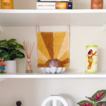 Shelf decorated with books, plants, candles, sculptures, hula girls, and tiki mug