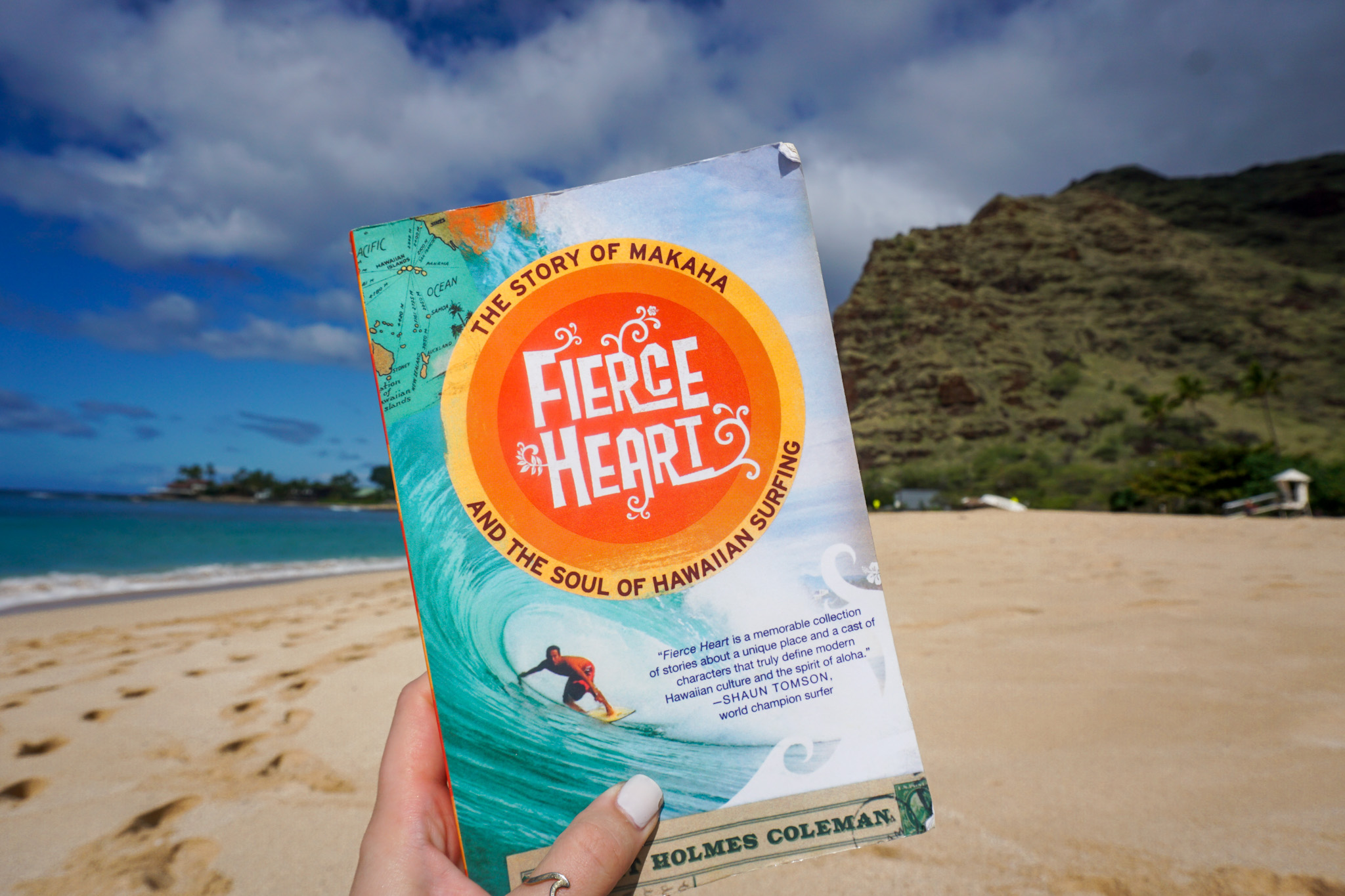 Photo of book (Fierce Heart) held up in front of mountain at Makaha Beach