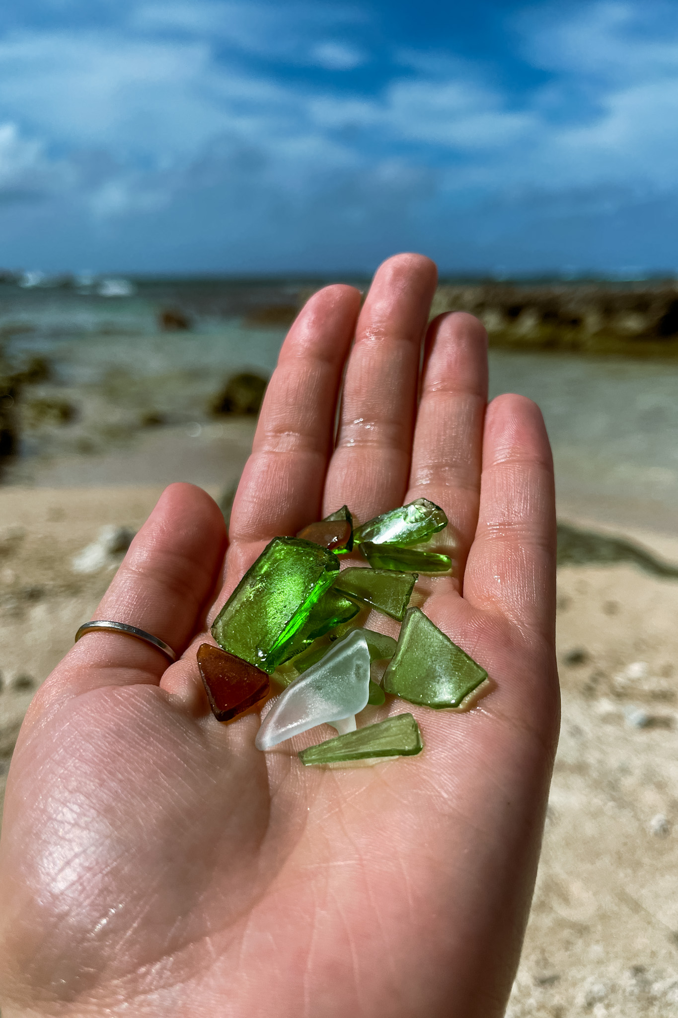 Hand holding pieces of green sea glass found on Hawaiian beach