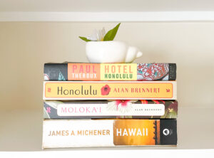 Stack of books including "Hotel Honolulu", "Honolulu", "Moloka'i", and "Hawaii"